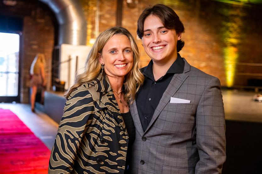 A woman wearing a patterned top smiles with a man in a grey checked blazer